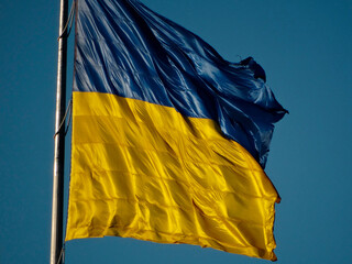 A blue flag with horizontal bands, lighter at the bottom and sides with yellow stripes, flying in a clear sky under favorable weather conditions