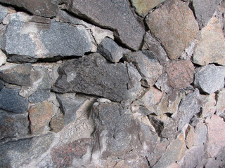Close-up image of an irregular, dry stone wall with gaps allowing light and creating shadows Grayish color palette