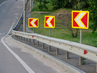 Image displays a road section with traffic merge signs, safety guardrail, and rural or suburban...