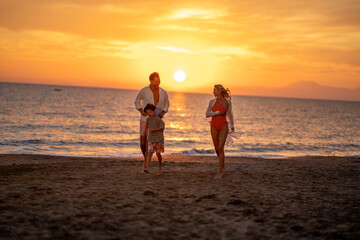 Fototapeta premium Description: A family having fun on the beach during sunset. They are playing together, enjoying the beautiful evening sky and ocean.