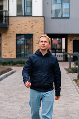 A Caucasian man in a jacket walks along the street along the houses