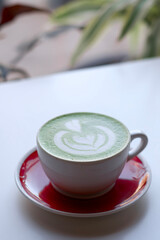 Ceramic Mug of Green Tea Matcha Latte Drink With Microfoam Art of Flower and Heart on White Cafe Table