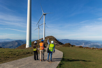 multiethnic Engineers walking and discussing next to wind turbines on mountain top