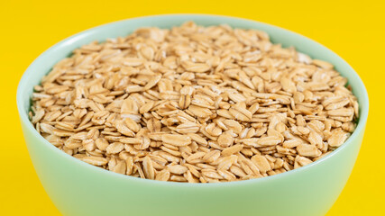Pastel green bowl filled with rolled oats against a bright yellow background. Perfect for healthy breakfast and organic lifestyle themes.