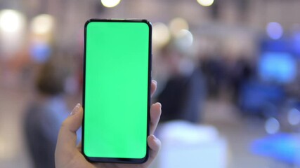 A hand is holding a smartphone that features a green screen intended for a mockup display