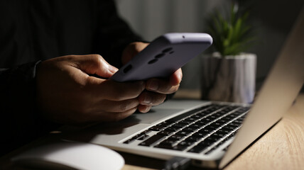 Programmer using smartphone and laptop working at night on cybersecurity project