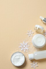 Winter skin care concept. Cosmetic products packaging design. Dropper bottle with serum, moisturizer cream jar and snowflakes on color background. Flat lay, top view.