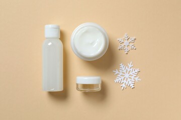 Winter skin care concept. Cosmetic products packaging design. Dropper bottle with serum, moisturizer cream jar and snowflakes on color background. Flat lay, top view.