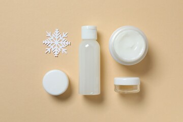 Winter skin care concept. Cosmetic products packaging design. Dropper bottle with serum, moisturizer cream jar and snowflakes on color background. Flat lay, top view.