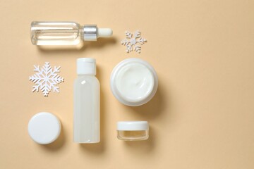 Winter skin care concept. Cosmetic products packaging design. Dropper bottle with serum, moisturizer cream jar and snowflakes on color background. Flat lay, top view.