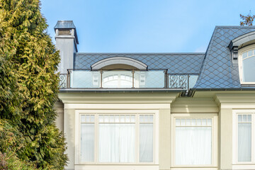 Top of grey stucco luxury house with shingle roof, red and yellow trees and nice windows in Summer in Vancouver, Canada, North America. Day time on June 2024.