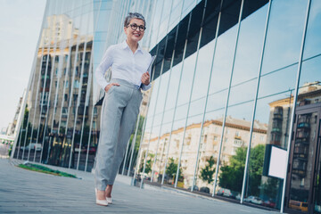 Confident mature businesswoman outdoors in urban cityscape, elegant in formalwear and smiling at success