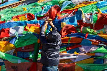 A pilgrim in a dark jacket adds colorful Tibetan prayer flags at Sun and Moon Mountain, a spiritual site in the Qinghai-Amdo region of Greater Tibet.