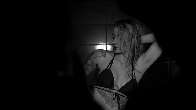 Sexy woman fashion model takes a shower in a swimsuit, posing for the camera. Monochrome photography.