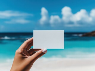 Woman hand holding a blank card with a beach and ocean in the background during the summer.