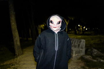An alien in a black robe appears in a forest at night.The alien looks at the camera with his hands...