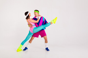 Energetic male and female duo in retro sportswear performing an athletic dance move.