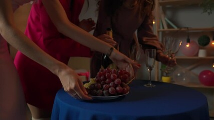 Group of young women friends and bride celebrating bachelorette party at home, bridesmaids preparing party snacks, putting champagne and fruits on the table.