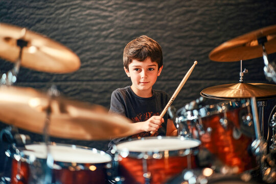 Young caucasian boy playing drum set in studio environment with focused expression