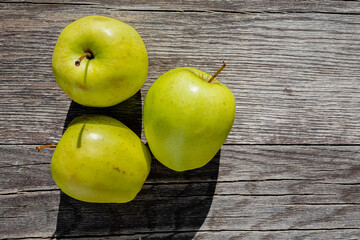 Green apples sit on an old tabletop made of weathered grey planks, creating a contrast between the freshness of the fruit and the worn texture of the surface that reflects years of use.