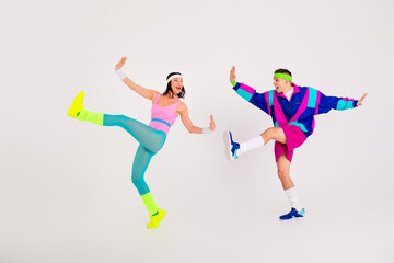 Energetic couple in vibrant retro sportswear performing dynamic aerobics moves on a white background.