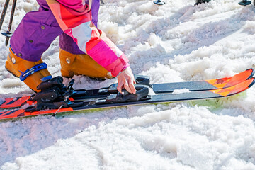 skier puts on his ski boots on a snowy slope on a sunny day. Active family vacation