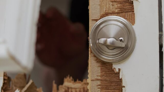 A hand reaches through a hole smashed on a white door and unlocks the latch.