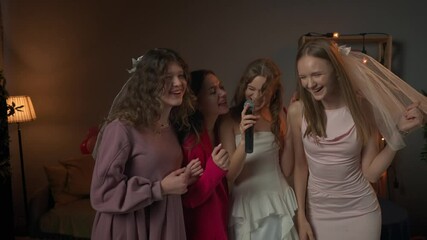 Group of young women friends and bride celebrating bachelorette party at home, bride and bridesmaids having fun, singing song in karaoke microphone.