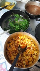 Mesa com panelas com macarrão cozido com molho de tomate, couve refogada, feijão cozido, e polenta.