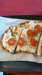 Pizza de queijo com tomate e orégano, sobre bandeja grafite, sobre mesa vermelha.
