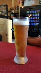 Um fino ou imperial, de portugal, sobre uma mesa vermelha, e imagens desfocadas ao fundo, do interior de um bar.