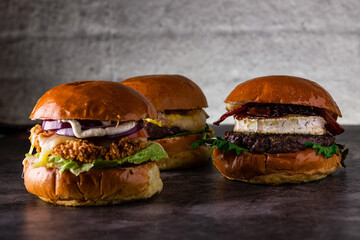 Trio of gourmet burgers with various toppings on a wooden table