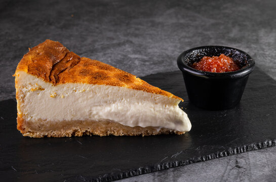 Slice of creamy cheesecake with guava on dark slate background