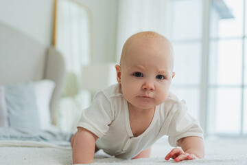 Happy baby. Cute little newborn girl with smiling face crawling on bed in bedroom. Infant baby resting playing lying down on blanket at home. Motherhood happy child childcare concept