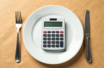 Diet concept with calculator on empty plate with fork and knife isolated on brown recycled paper background with copy space, food spending costs concept