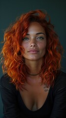 Fototapeta premium Portrait of a woman with vibrant red curly hair and subtle makeup, looking directly at the camera against a dark green background.