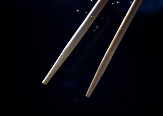 Chopsticks dipped in water create bubbles near a dark background