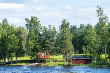 Obraz premium Red building and a small boathouse next to a river on a summer day near Kuusamo, Northern Finland