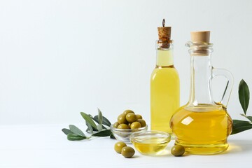 Bottles of fresh olive oil and olives with leaves on white background