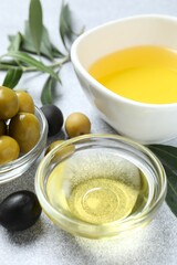 Bowl of fresh olive oil and olives with leaves on the table