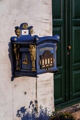 Blue post mailbox on white wall.
