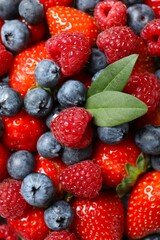 Different fresh ripe berries in bowl on wooden table, top view