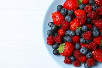 Different fresh ripe berries in bowl on wooden table, top view