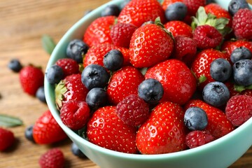Different fresh ripe berries in bowl on wooden table