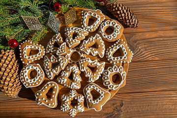 Iced Christmas Cookies with Rustic Decorations. Decorative gingerbread cookies with white icing shaped as bells, trees, and hearts, placed on a wooden background with pinecones.