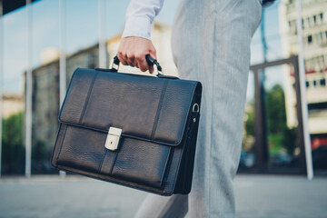 Confident business professional carrying leather briefcase in an urban cityscape during daylight,...