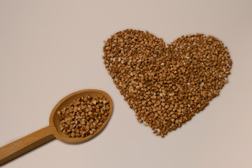 A heart formed from buckwheat is accompanied by a wooden spoon filled with buckwheat, placed nearby.