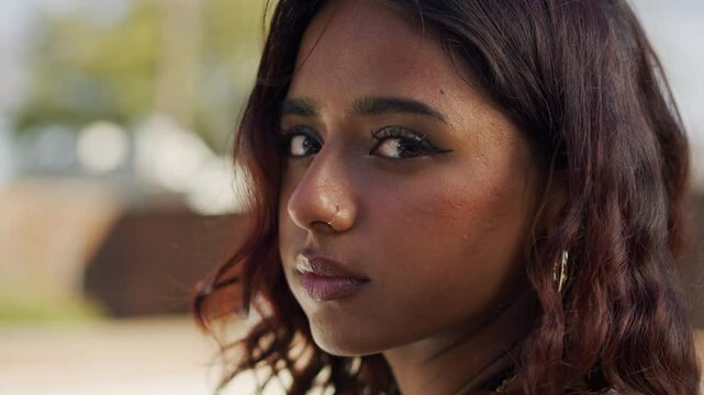 Close-up portrait of a woman looking into the camera and smirking outside.