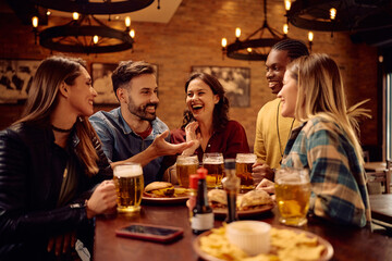 Cheerful group of friends talking while drinking beer in bar.