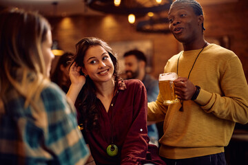 Happy friends communicating while gathering for drink in pub.